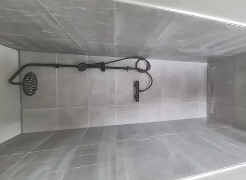 Inloopdouche met betonlook-tegels, matzwart tapwerk en een lange douchegoot langs de wand