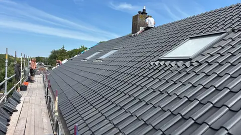 Een dakdekker werkt het loodwerk rond de schoorsteen af